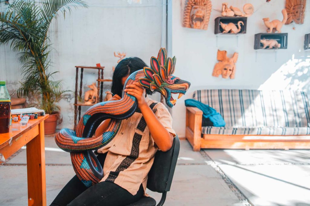 Young girl painting a wooden dragon-like creature with colorful patterns in Mexican style