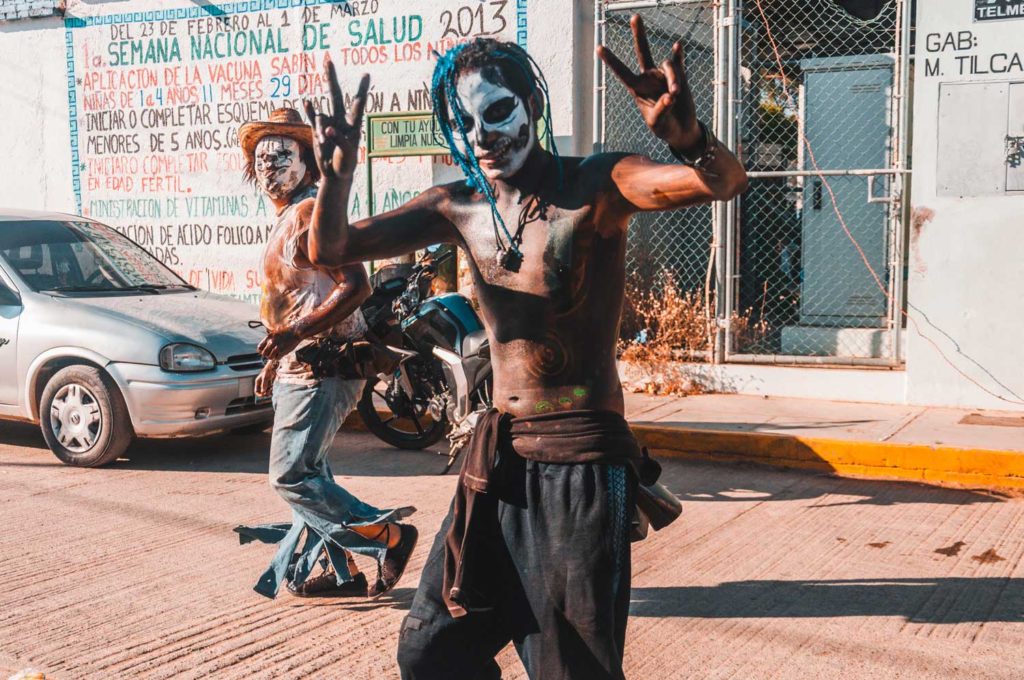 Young Mexican With Skull Make Up Showing Peace Sign, With A Man In Clown Make Up Behind Him