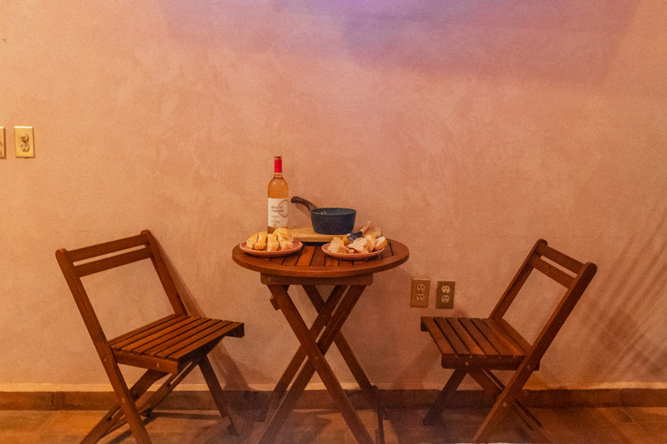 Two chairs and a table int he middle with bread, wine and cheese fondue