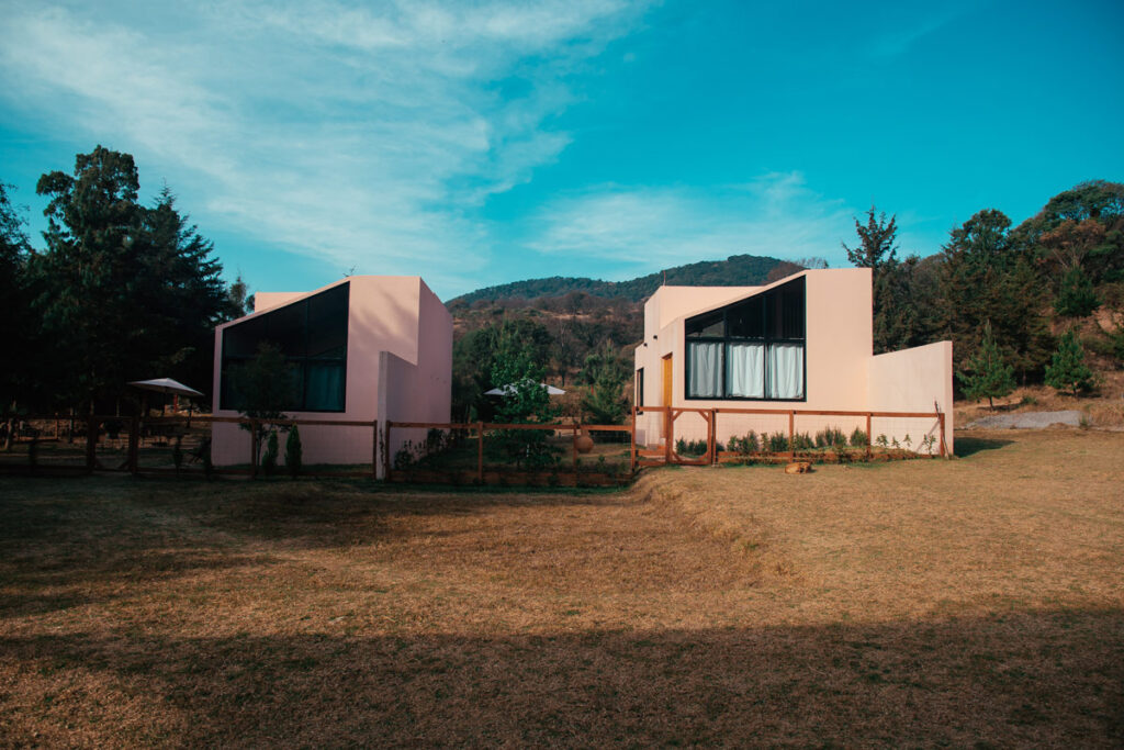 Two pink Airbnb cabins sitting next to each other on a bright sunny day with blue skies.