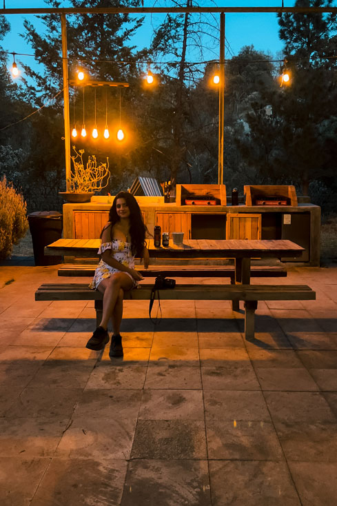 Indian girl sitting at the bench of the shared kitchen at La Comuna with fairy lights on top.