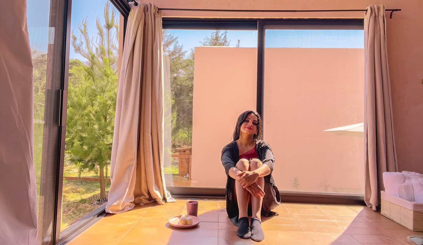 Indian girl in black robe siting in front of a window with cupcakes on her left