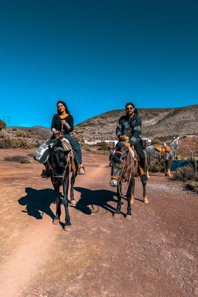 A girl riding a black horse and a guy riding a brown horse, with blue skies and desert in the background
