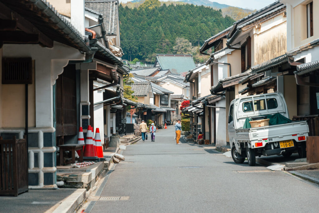 Old couple walking in the streets of Uchiko, with Edo-era buildings on both side and a Japanese truck on the right.