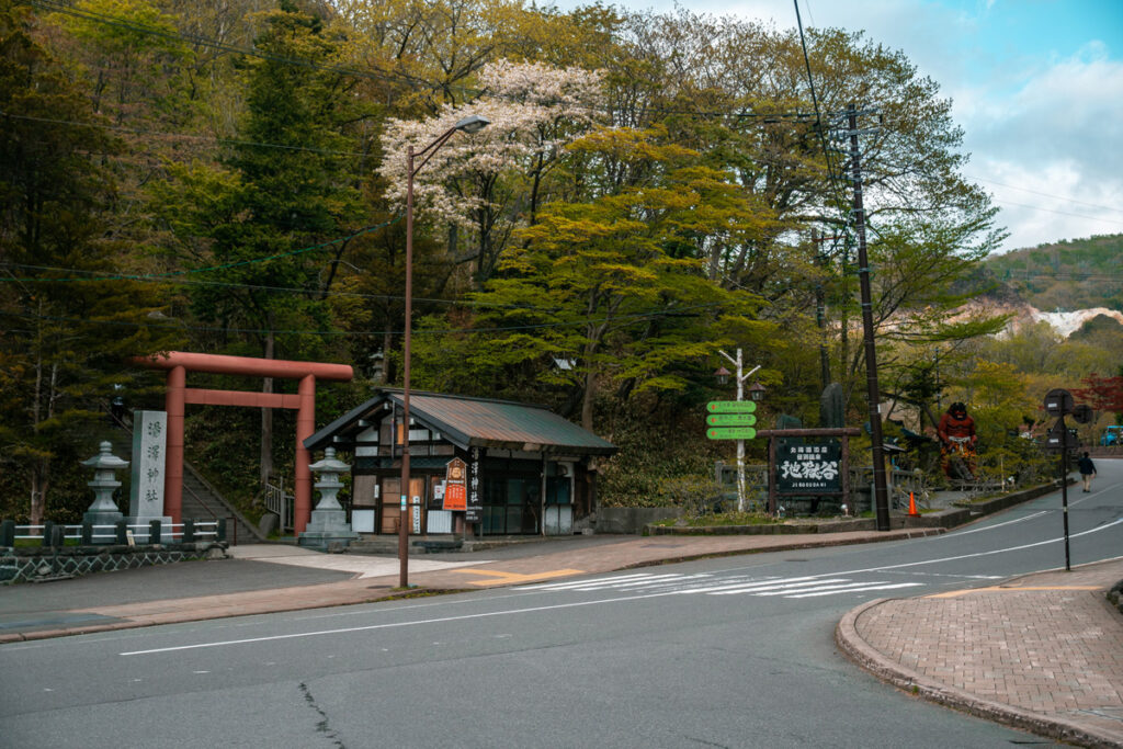 Tori entrance to a shrine up on a hill, with a red demon on the right, in Noboribetsu Onsen,