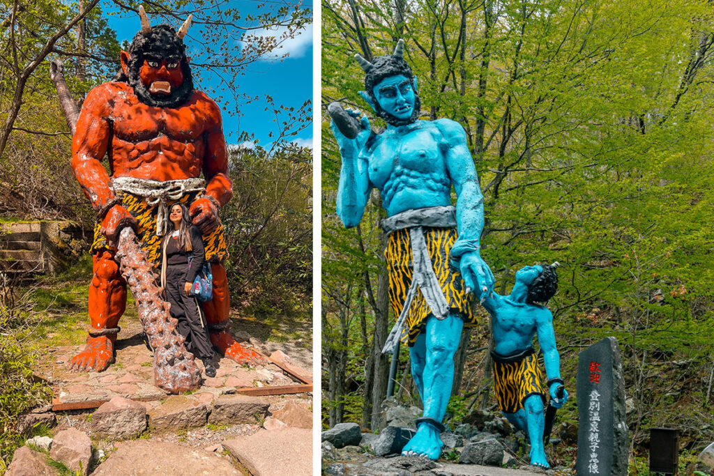 Left: Red demon statue with a staff in his hand, standing with travel blogger Himanshi posing in Noboribetsu Onsen, with forests around.

Right: Blue father and son demon duo statue 