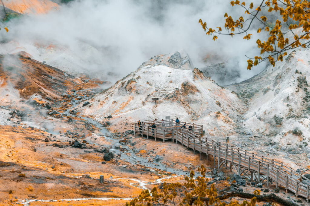Noboribetsu Onsen's Hell Valley with people walking in the boardwalk and sulphur fog all around