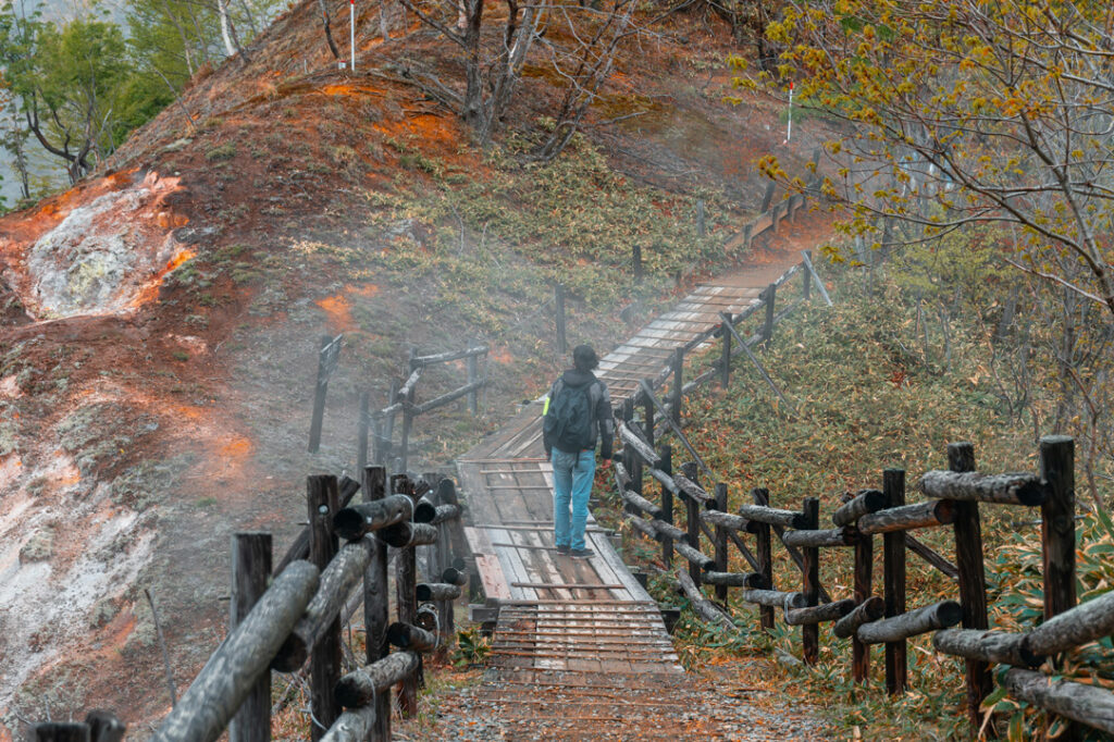 Man walking with a backpack on the boardwalk of Noboribetsu onsen's hell valley.